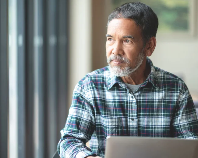 male hispanic adult working at laptop and looking out window