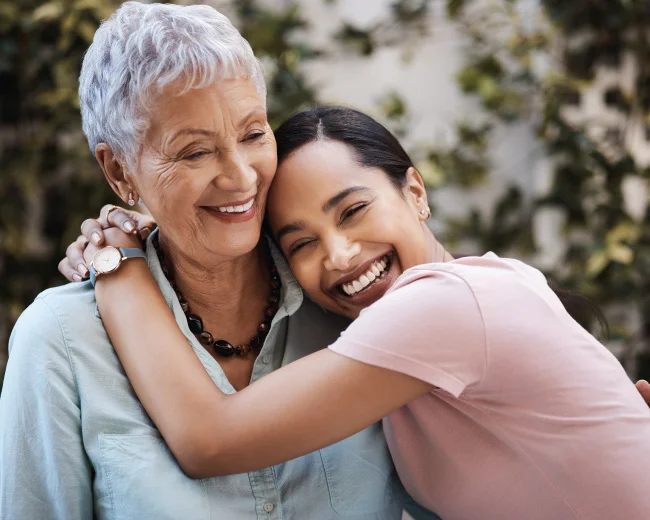 hispanic grandmother and adult daughter smiling together while hugging tightly