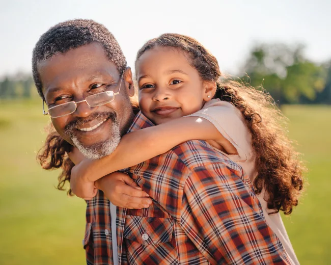 grandfather carrying granddaughter on his shoulders, both smiling